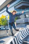 Joven skateboarder urbano masculino equilibrado en la parte superior de la barrera de hormigón - foto de stock