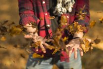 Young man throwing autumn leaves in air, mid section — Stock Photo