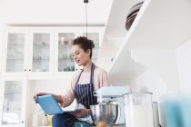 Young female baker sitting on kitchen counter looking at laptop — Stock Photo