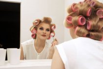 Young woman in curlers putting on make-up — Stock Photo