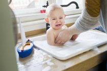 Mother removing upset baby son from kitchen sink — Stock Photo