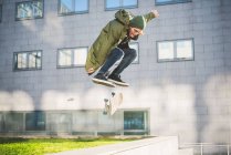 Young male urban skate boarder skateboarding mid air over wall — Stock Photo