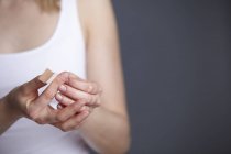 Recortado de cerca tiro de mujer joven aplicando yeso adhesivo a su propio dedo - foto de stock