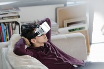 Молодий чоловік на дивані в гарнітурі віртуальної реальності — стокове фото