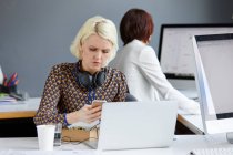 Designer feminina olhando para smartphone durante o almoço de trabalho na mesa de escritório — Fotografia de Stock