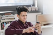 Jeune homme sur canapé textos sur smartphone — Photo de stock