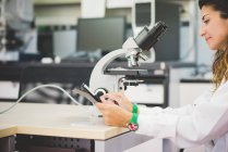 Female scientist using digital tablet and optical microscope — Stock Photo