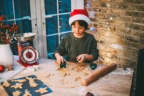Menino em chapéu de Santa preparando biscoitos de Natal no balcão da cozinha — Fotografia de Stock