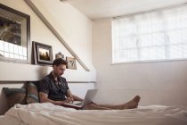Hombre en la cama usando el ordenador portátil - foto de stock