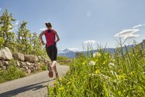 Jovem mulher correndo ao longo da estrada rural, visão traseira, Meran, Tirol do Sul, Itália — Fotografia de Stock
