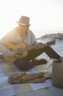 Joven tocando la guitarra en una manta de picnic en la playa, Cape Town, Western Cape, Sudáfrica - foto de stock