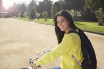 Середня доросла жінка сидить на велосипеді в парку, дивлячись на камеру посміхаючись — стокове фото