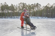 Boy pushing friend on kicksled across frozen lake, Gavle, Sweden — Stock Photo