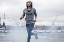Young female runner running  on stormy dockside — Stock Photo