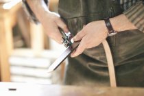 Trabajador masculino en taller de cuero, perforando agujeros en el cinturón de cuero, sección central, primer plano - foto de stock