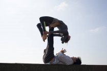 Uomo e donna sagomati che praticano yoga acrobatico sulla parete contro il cielo blu — Foto stock