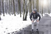Young man taking a break from exercise, in snowy forest — Stock Photo
