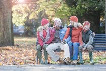 Семья, сидящая вместе на скамейке в парке, смеющаяся — стоковое фото