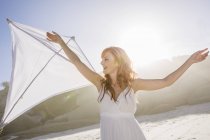 Red haired woman on beach holding kite looking away smiling — Stock Photo