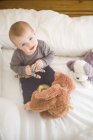 Baby girl sitting on bed holding soft toys looking up at camera — Stock Photo