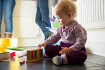 Девочка, сидящая на полу кухни и играющая с игрушками — стоковое фото