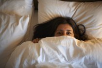 Portrait of mature woman peeking from hotel bed at night — Stock Photo
