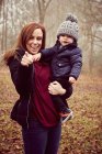 Femme adulte moyenne portant tout-petit fils et pointant dans la forêt d'automne — Photo de stock