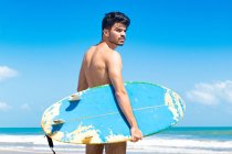 Junger Mann steht am Strand, hält Surfbrett, fortaleza, ceara, brasilien — Stockfoto