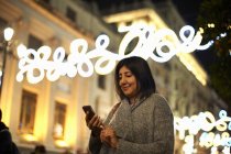 Frau mit Smartphone, dekorative Lichter im Hintergrund, Sevilla, Spanien — Stockfoto