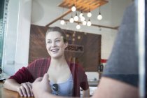 Молода жінка сидить з чоловіком у кафе, посміхаючись — стокове фото