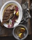 Whole grilled snapper on serving tray with salad leaves and lemon — Stock Photo