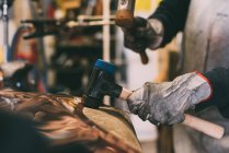 Mãos de metalúrgico martelando cobre em oficina de forja — Fotografia de Stock
