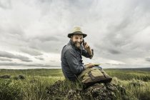 Retrato de senderista varón maduro sentado en las rocas usando un teléfono inteligente, Cody, Wyoming, EE.UU. - foto de stock