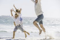 Pai e filhos pulando na praia — Fotografia de Stock