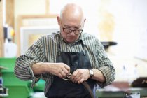 Male worker in leather workshop, polishing belt buckle — Stock Photo