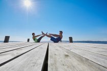 Mid distance view of couple on pier face to face doing sit ups — Stock Photo