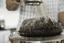 Homem peneirando açúcar de confeiteiro sobre bolo — Fotografia de Stock