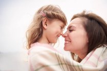 Happy mother and daughter wrapped in blanket, rubbing noses — Stock Photo