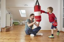 Father holding punchbag for son at home — Stock Photo