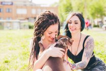 Jeunes femmes tatouées jouant avec pit bull terrier dans un parc urbain — Photo de stock