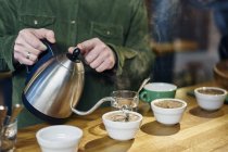 Мужчина наливает кипящую воду в кофейные чашки для дегустации на стойке кафе — стоковое фото