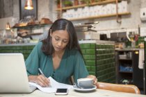 Середня доросла жінка робить документи за столом кафе — стокове фото