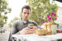 Чоловік в кафе на тротуарі дивиться на смартфон — стокове фото