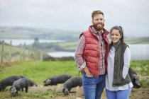 Couple on pig farm looking at camera smiling — Stock Photo