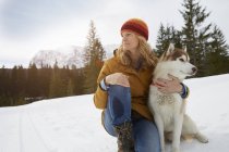 Frau sitzt mit Husky in verschneiter Landschaft, Elmau, Bayern, Deutschland — Stockfoto