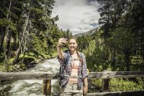 Молода жінка мандрівного на місток беручи смартфон selfie, червоний Lodge, штат Монтана, США — стокове фото