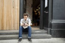 Kellner macht Pause auf Café-Treppe und schaut aufs Smartphone — Stockfoto