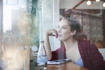 Молодая женщина сидит в кафе, смотрит в окно — стоковое фото