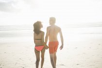 Vista trasera de pareja joven en traje de baño paseando por la playa soleada, Cape Town, Western Cape, Sudáfrica - foto de stock