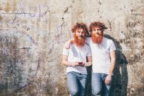 Portrait of young male hipster twins with red beards standing in front of wall — Stock Photo